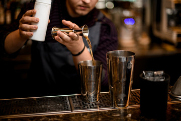 Male bartender pouring a alcoholic drink from the jigger to a steel shaker