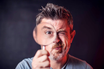 Man holds magnifier in front of eye on the black background