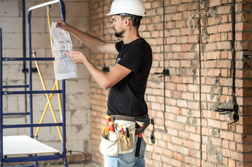 Builder handyman with construction tools, looking at the drawings on the construction site.