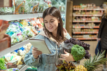 A young woman with a notebook buys groceries in the supermarket.