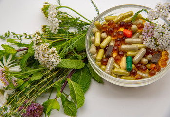 A bowl with various capsules and tablets, medicinal and aromatic herbs.