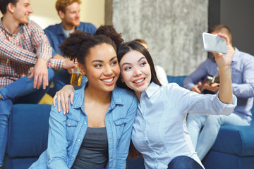 Group of friends having party indoors fun together two girls taking selfie pictures
