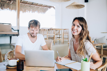 Obraz premium Portrait of cheerful female digital nomad sitting at cafeteria table with happy hasbund and spending time togetherness for planning next trip doing online laptop ticketing on touristic website