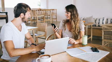 Happy woman reading email received on modern smartphone while spending time with hasband, cheerful male and female freelancers discussing content text of web publication posted in social network