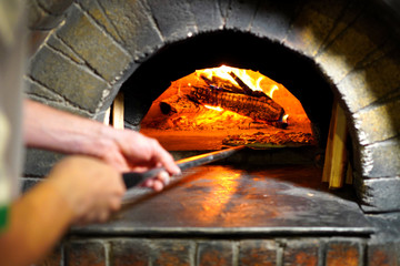 Pizza maker hands take out pizza from stone oven
