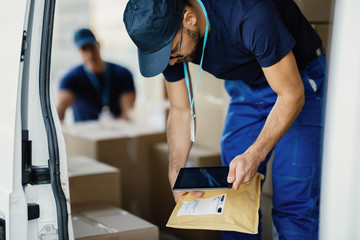 Young courier using digital tablet and scanning package labels in a delivery van.