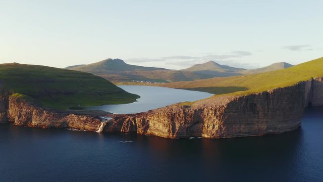 Aerial drone video flying over Bosdalafossur waterfall on Sorvagsvatn lake in sunset time. Vagar island, Faroe Islands, Denmark. UHD 4k video