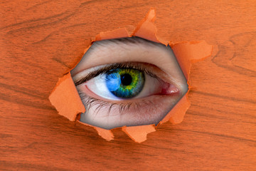 the close up of eye looking through the torn paper hole