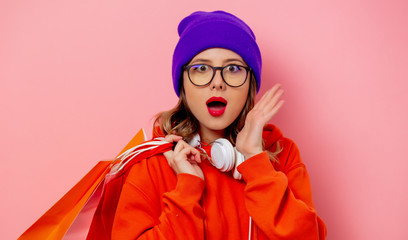 Obraz premium Style girl in orange hoodie and purple hat with shopping bags on pink background