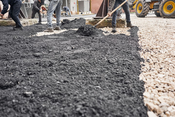 Laying new asphalt, covering the pit, on the rubble. Workers carry in shovels and using asphalt lute for smooth, hot asphalt.