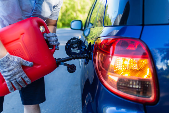 Filling The Machine From The Canister Into The Neck Of The Fuel Tank. Man Pouring Fuel Into The Gas Tank Of His Blue Car From A Red Petrol Canister.