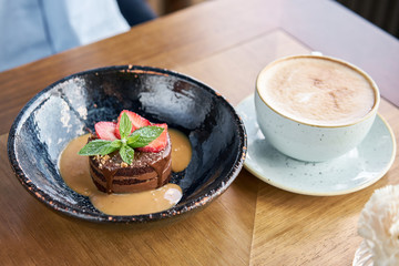 Woman eats chocolate sponge cake, with caramel, decorated with strawberries and mint leaf. Breakfast in the cafe, morning coffee. on wooden table. Restaurant menu