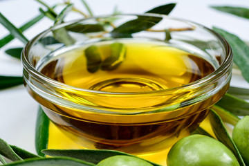 Olive oil. Glass transparent bowl with extra virgin greek olive oil among olive leaves and olives. Close-up macro, high resolution.
