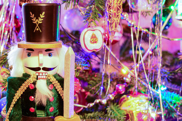 Nutcracker soldier under decorated colorful Christmas tree. Traditional Xmas festive wooden toy, close-up.