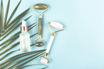 Trendy beauty tools and treatment. Pink and green jade rollers on palm leaf. Skincare concept.