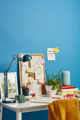 Cozy workplace with notebooks, beverage, desk lamp and different notes on wall near, reminding what to do, writing daily tasks. Students desktop with necessary supplies. Modern home study room