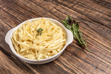 Homemade fettuccine with bechamel sauce in a white plate, rustic wooden table background, soft light - Italian food style