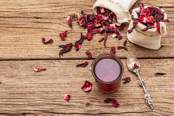 Hot hibiscus tea. Dry petals, linen sacks. Healthy food and self-care concept. Old wooden boards backgrounds