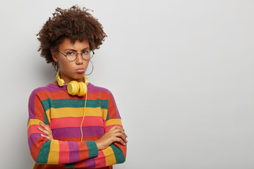 Offended upset curly woman with arms folded, gloomy face expression, stands sullen and...