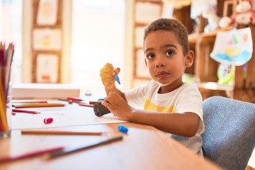 Beautiful african american toddler sitting painting car toy using marker pen on desk at kindergarten