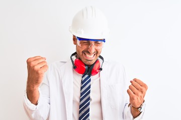Young chemist man wearing security helmet and headphones over isolated background very happy and excited doing winner gesture with arms raised, smiling and screaming for success. Celebration concept.