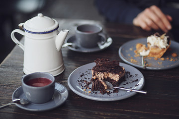 A metal teapot with rose tea in a restaurant. Tea party with chocolate dessert in a cafe. Vitamin raspberry tea with mint and cheesecake. Sweets, desserts with a hot drink.Gray dishes and wooden table