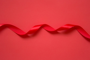 Red satin twisted ribbon on red background. Photo with copy blank space.