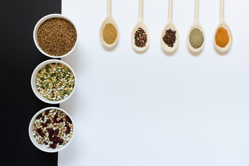 Collection of cooking ingredients variety of grains and legumes with spicing herbs in wooden spoons on white and black background. Photo with copy blank space.
