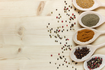 Various herbs on wooden spoons on wooden board background. Black pepper, aromatic cloves, mustard, pepper peas, paprika. Photo with copy blank space.