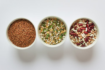 Three bows with variety of legume grains buckwheat, white red beans on white background.