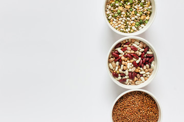 Three bows with variety of legume grains buckwheat, white red beans arranged on the right of image. Photo with copy blank space.