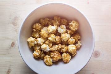 Handful of sweet popcorn with caramel glaze in ceramic bowl on wooden background.