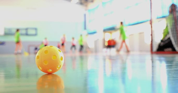 Floorball match of small floorball players. Children play floorball match in indoor hall. Intentionally focused on the ball in the foreground. Players in the background intentionally out of focus.