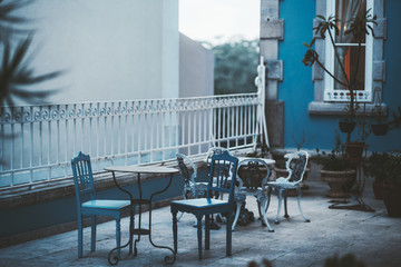 An evening shot with a shallow depth of field of a small patio in Sintra, Portugal, with two antique dining tables outdoors with a selective focus on two old elegant carved chairs in the front