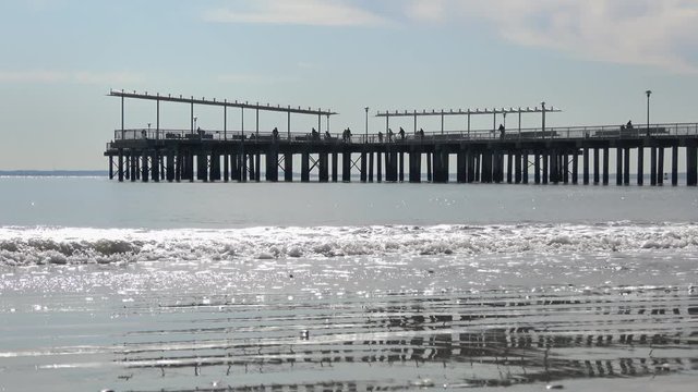 4K. Ultra HD. Images of tourists and locals walking on a pier, with calm waves crashing into the foreground pier. Coney Island Pier, Brooklyn, New York. Travel and nature concept.