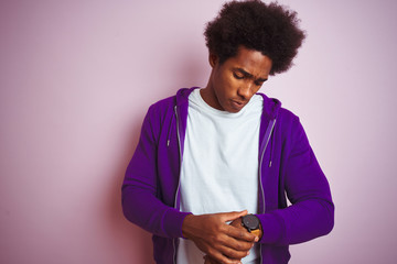 Young african american man wearing purple sweatshirt standing over isolated pink background Checking the time on wrist watch, relaxed and confident