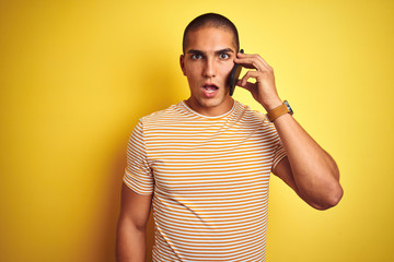 Young handsome man talking using smartphone over yellow isolated background scared in shock with a surprise face, afraid and excited with fear expression