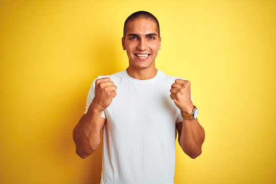 Young caucasian man wearing casual white t-shirt over yellow isolated background celebrating surprised and amazed for success with arms raised and open eyes. Winner concept.