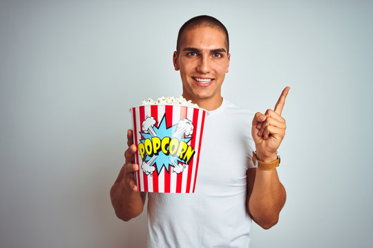 Young handsome man eating popcorn over white isolated background very happy pointing with hand and finger to the side