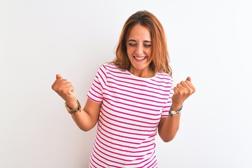 Young redhead woman wearing striped casual t-shirt stading over white isolated background very happy and excited doing winner gesture with arms raised, smiling and screaming for success