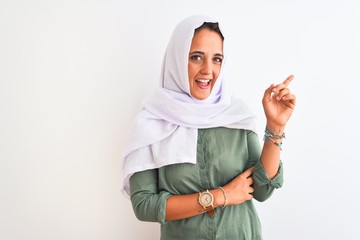 Young beautiful Arab woman wearing traditional Muslim hijab over isolated background with a big smile on face, pointing with hand and finger to the side looking at the camera.