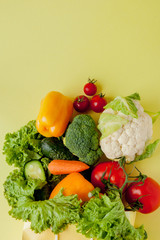 Organic vegetables broccoli cucumbers bell peppers apples in brown paper Kraft grocery bag on yellow background. Healthy diet dietary fiber vegan plastic free concept. Poster banner