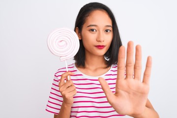 Young beautiful chinese woman eating lollipop standing over isolated white background with open hand doing stop sign with serious and confident expression, defense gesture