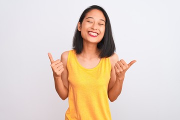 Young chinese woman wearing yellow casual t-shirt standing over isolated white background success sign doing positive gesture with hand, thumbs up smiling and happy. Cheerful expression and winner