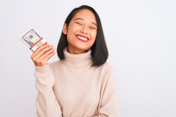 Young beautiful chinese woman holding dollars standing over isolated white background with a happy face standing and smiling with a confident smile showing teeth