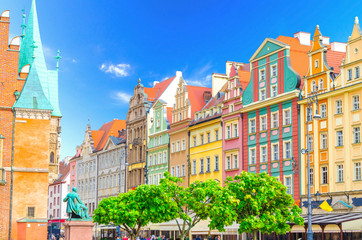 Row of colorful buildings with multicolored facade and wall of Old Town Hall building on cobblestone Rynek Market Square with green trees in old town historical city centre of Wroclaw, Poland
