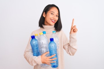 Young beautiful chinese woman recycling plastic bottles over isolated white background surprised...