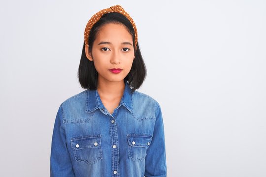 Young Beautiful Chinese Woman Wearing Denim Shirt Standing Over Isolated White Background With Serious Expression On Face. Simple And Natural Looking At The Camera.