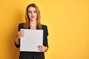Naklejka premium Young redhead businesswoman with clear eyes holding banner over isolated yellow background with a confident expression on smart face thinking serious