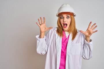 Redhead caucasian woman engineer wearing safety helmet over isolated background celebrating crazy and amazed for success with arms raised and open eyes screaming excited. Winner concept